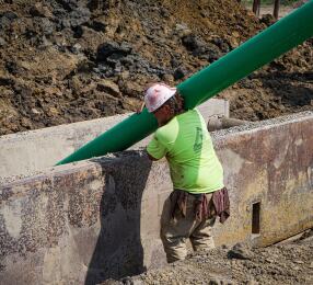 Man holding a large pipe installing it into a concrete trench.