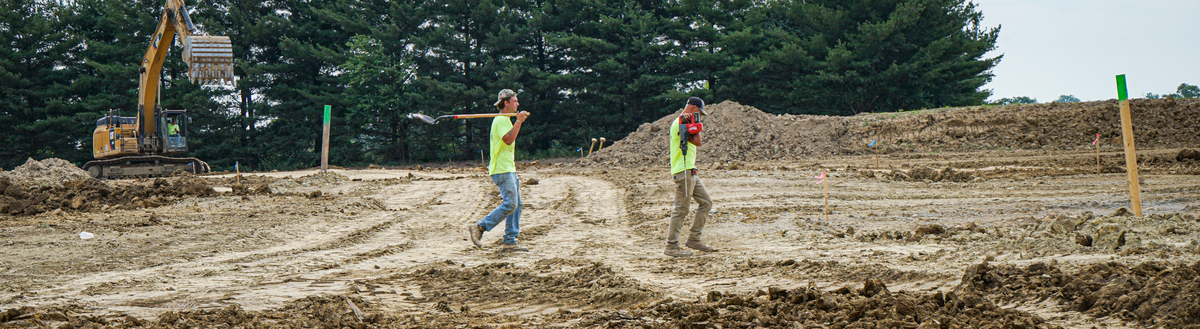 two men walk across a construction site carrying tools