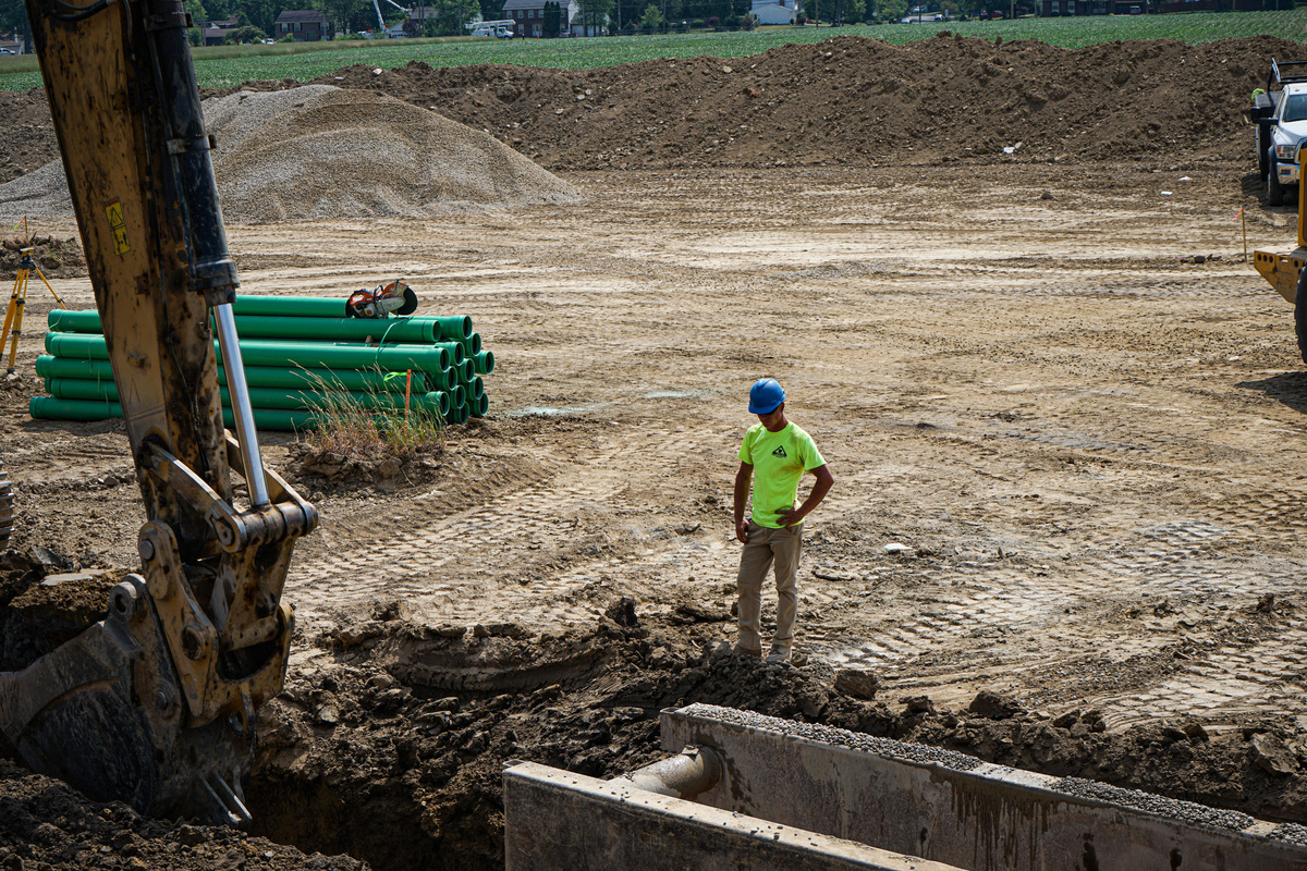 a construction worked stands next to a whole and observes a backhoe