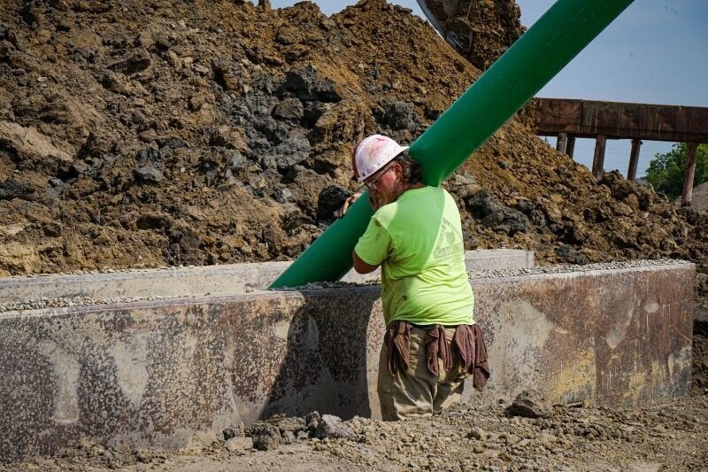 A worker guides a large piece of piping into a hole