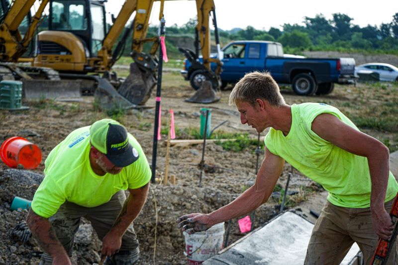 Two workers lean over freshly laid concrete