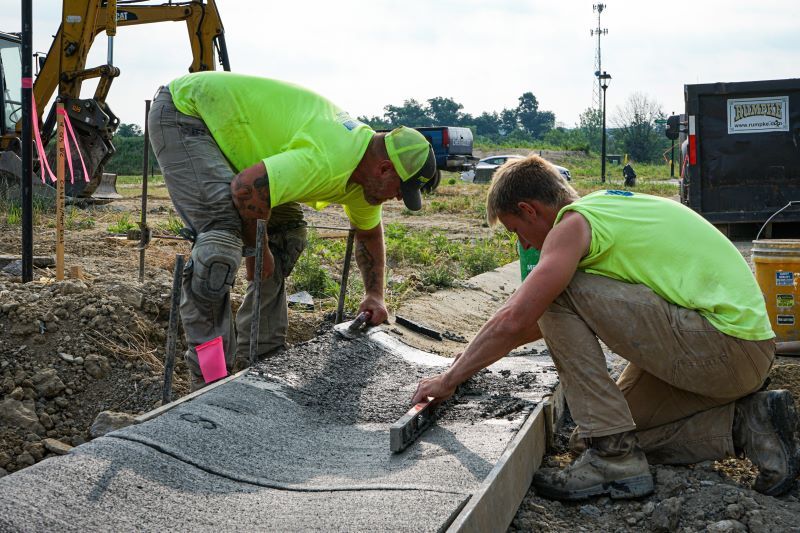 Men in yellow shirts laying down concrete.